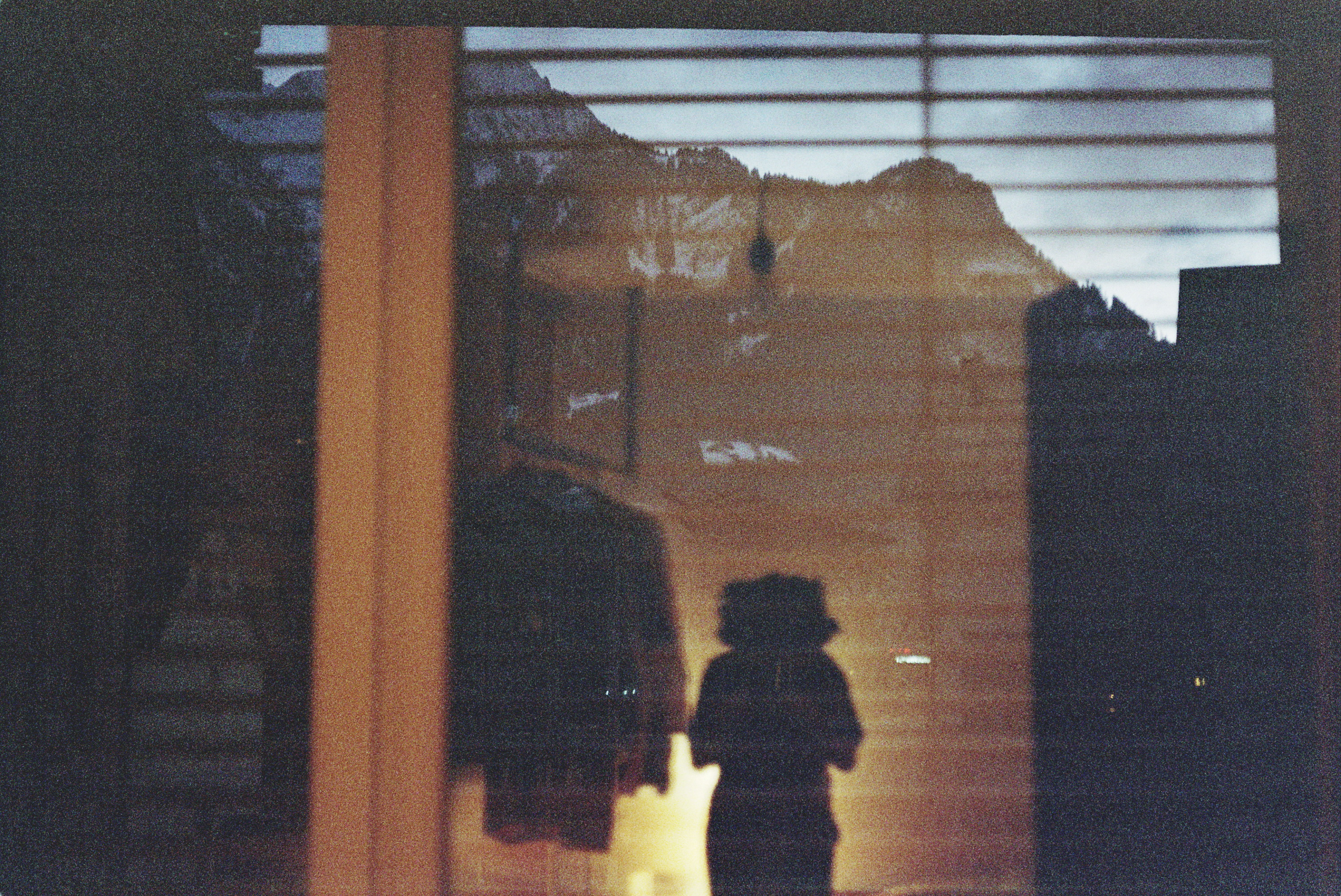Ta'Yali's outline reflected in a window. Behind the window alpine mountains of Bludenz in the dusk are visible. 