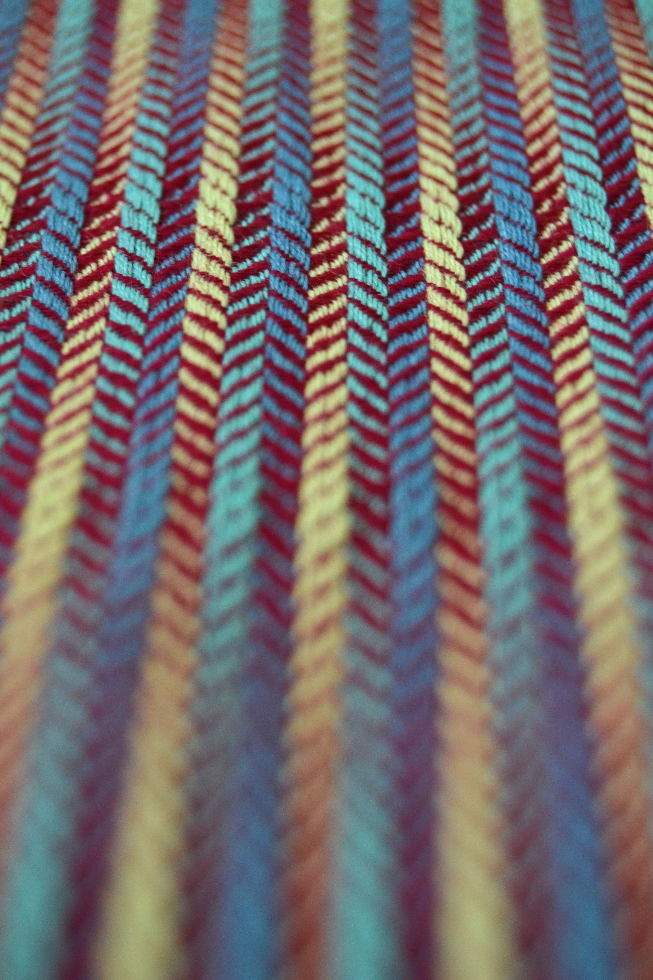 A picture of a fabric with perspective distortion from the front to the back. Vertical lines in cyan, yellow and blue are overlaid with a horizontal deep red gradation.