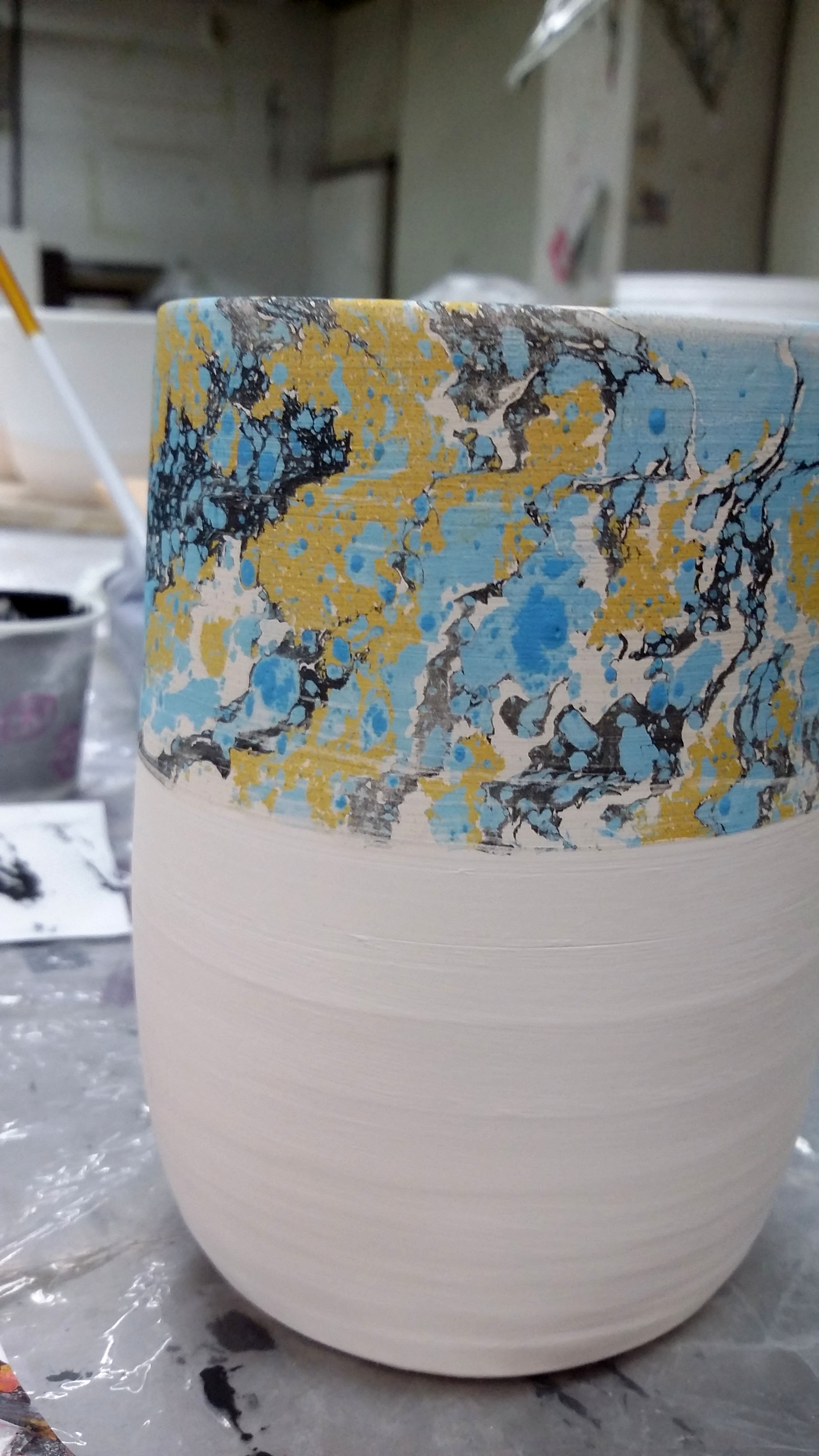 An vessel with the upper half marbled in lightblue, black and ochre, against the background of a workshop.