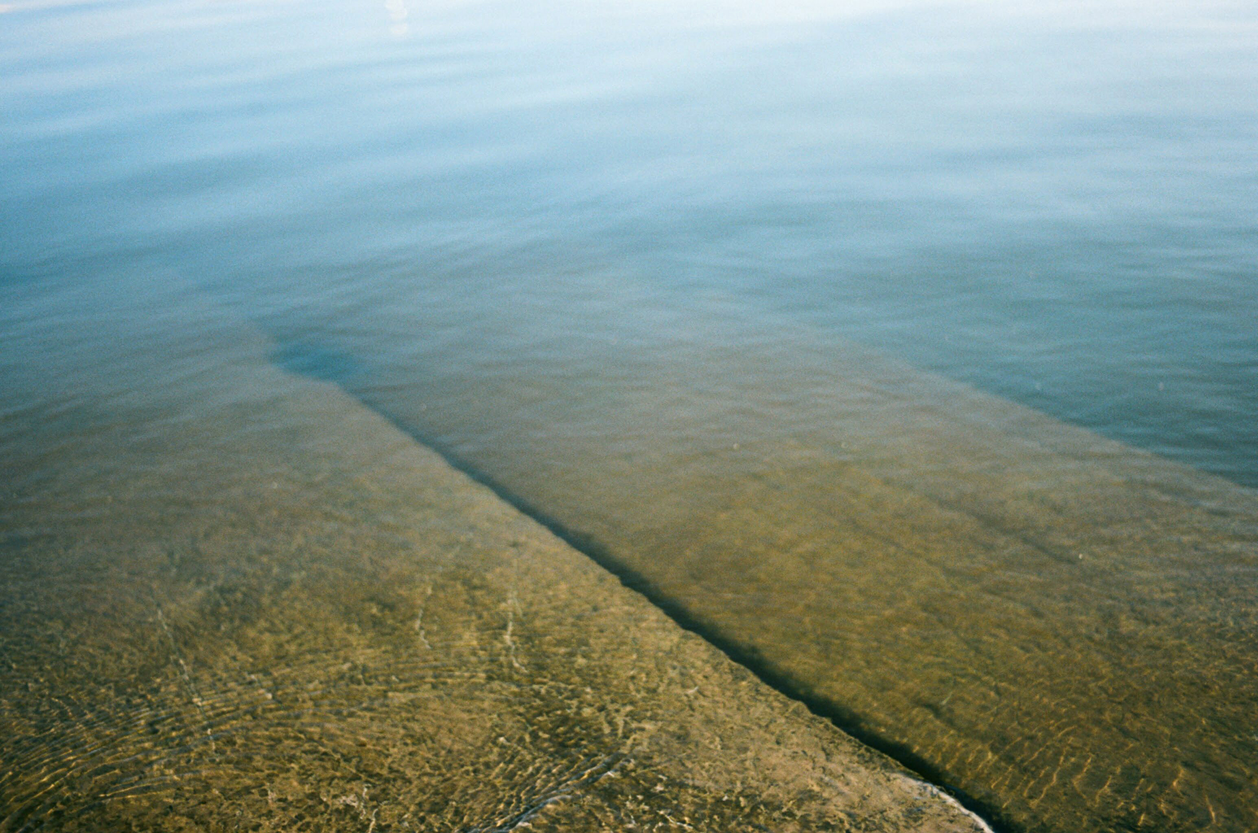 Birdeye-persepective onto brown greenish stone stairs at the front of the picture gradually disappearing into lightblue calm water towards the back of the picture.