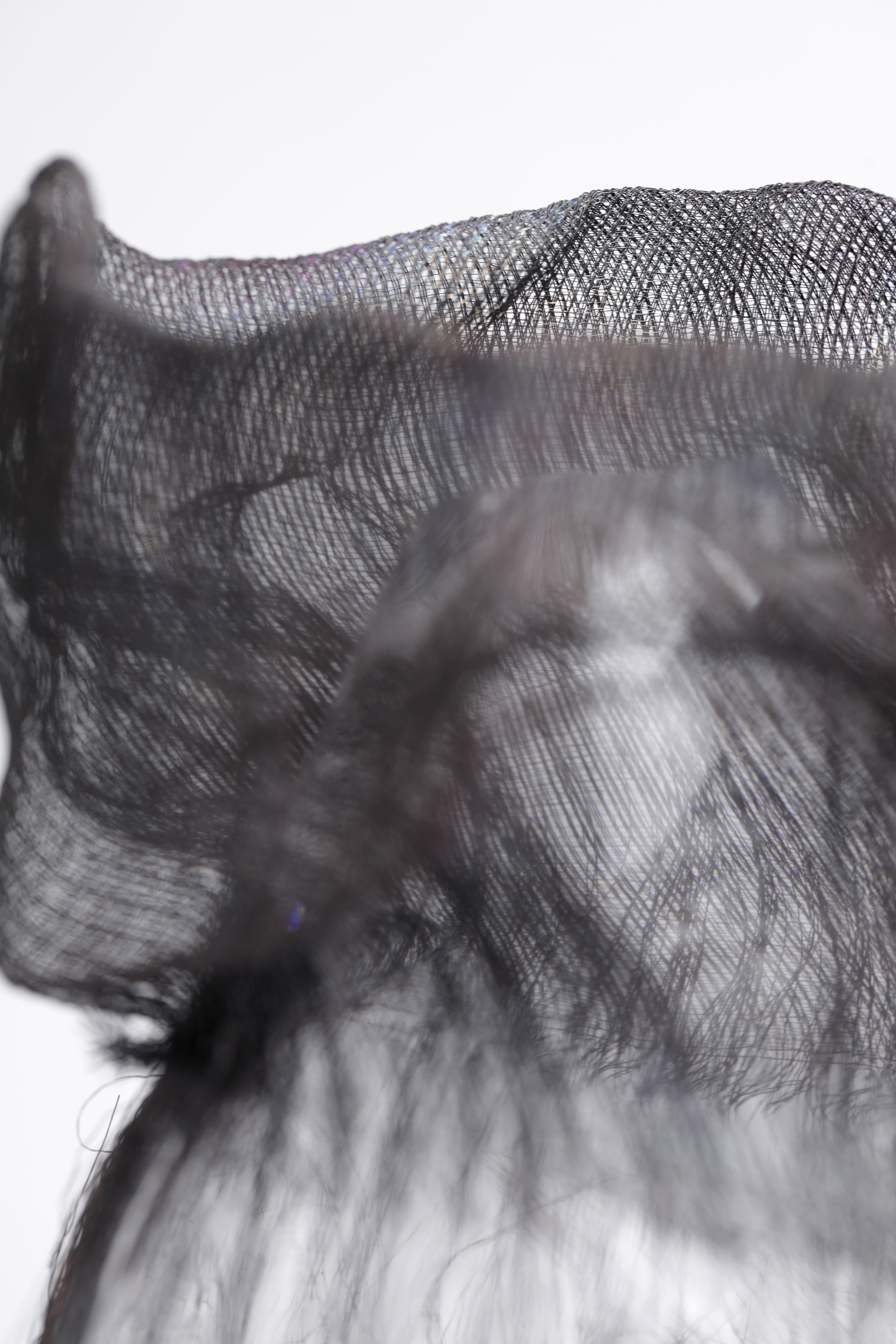 A layered piece of partly transparent fabric with cone-shaped glass showing through the middle. Photographed against a white background.