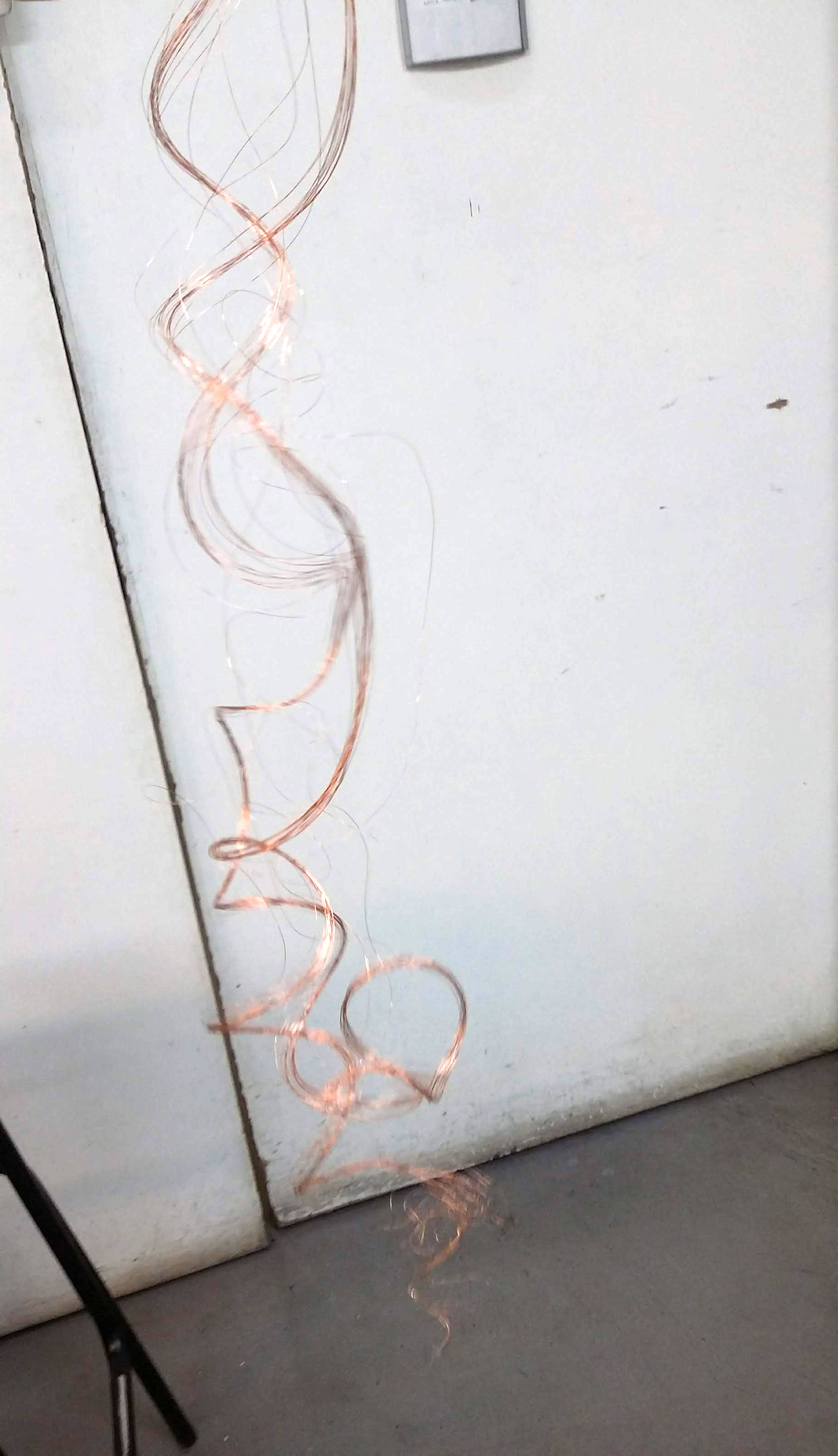 A shiny curled yarn falling from the top of the picture to the botom. Against the background of a white door and a grey floor.